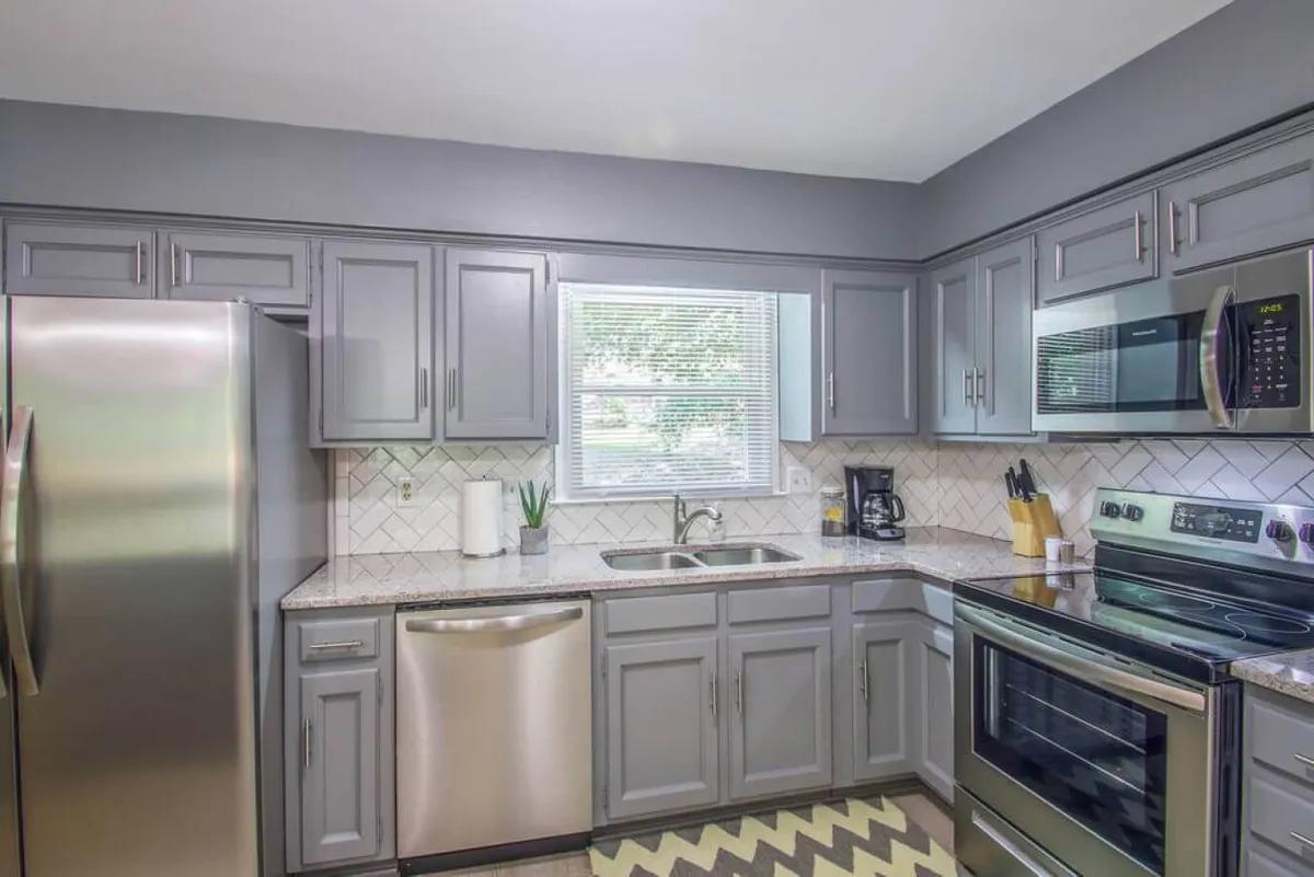 This image features a contemporary kitchen equipped with stainless steel appliances, a spacious granite countertop, a kitchen sink, and a window that allows ample natural light to brighten the space. The overall layout is open and inviting, making it ideal for meal preparation and social interaction.