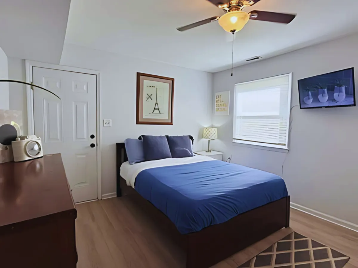 This bedroom scene highlights a plush bed with blue bedding, soft lighting from a nightstand lamp, tasteful artwork, and a flat-screen TV. The atmosphere is inviting and relaxing, ideal for unwinding after a day of exploring.