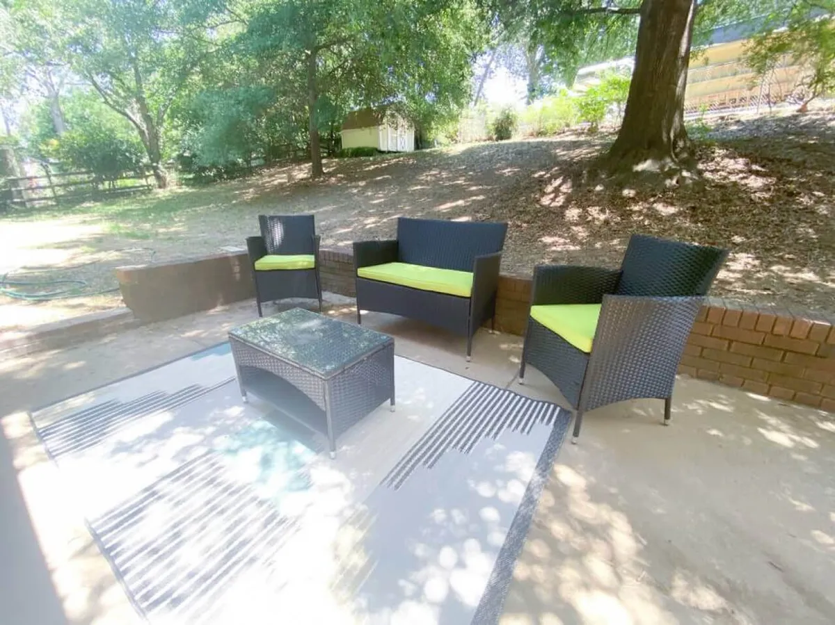 An inviting outdoor seating arrangement with a coffee table and area rug is nestled in a backyard rich with greenery. The scene is set for relaxation, reading, or entertaining guests, with nature providing a tranquil backdrop. The atmosphere is both social and serene, ideal for various activities throughout the day.