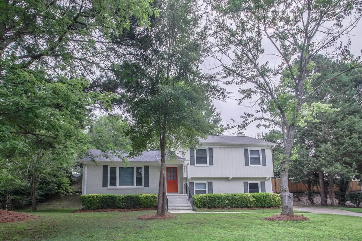 A welcoming shot of a home's front entrance with a landscaped yard, large windows, and mature trees. The inviting path and yard suggest space for outdoor gatherings, play, and relaxation after a day of adventure.