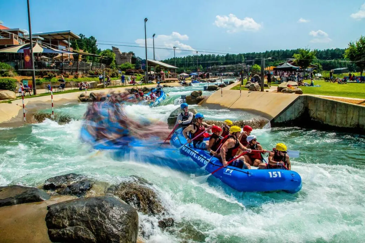A group of friends is seen white-water rafting down rushing waters, surrounded by dramatic rock formations and viewing areas. The image brims with energy, camaraderie, and adventure—showcasing group activities and memorable experiences.