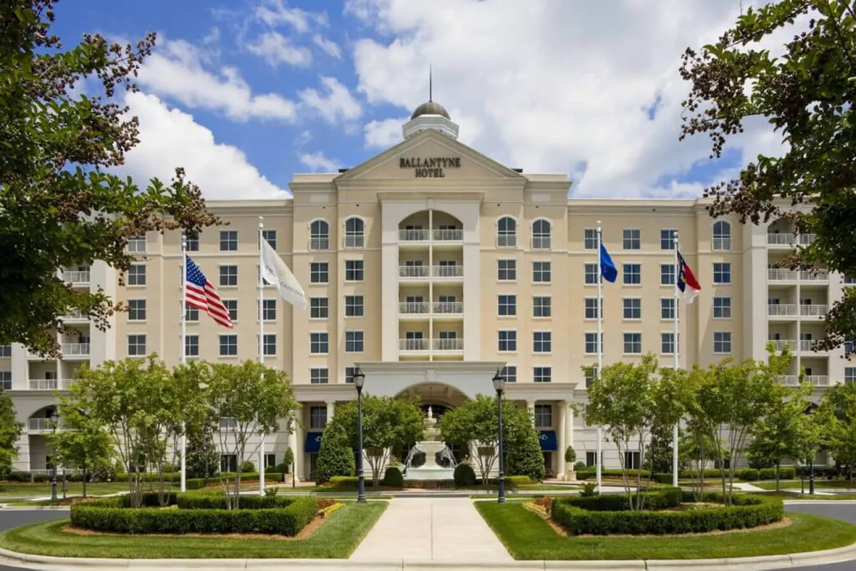 An elegant exterior shot of a hotel facade, complete with flags, a welcoming fountain, and beautifully landscaped gardens. The inviting atmosphere suggests a perfect place to gather before or after city exploration.